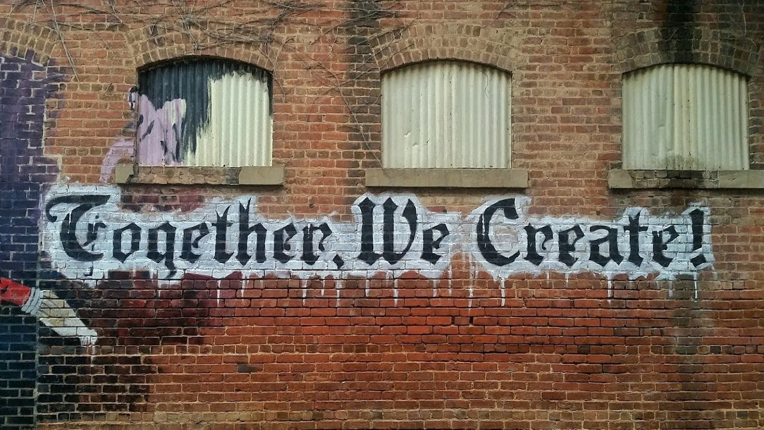 Graffiti on a brick wall with the phrase 'Together We Create' painted in large, stylized letters.